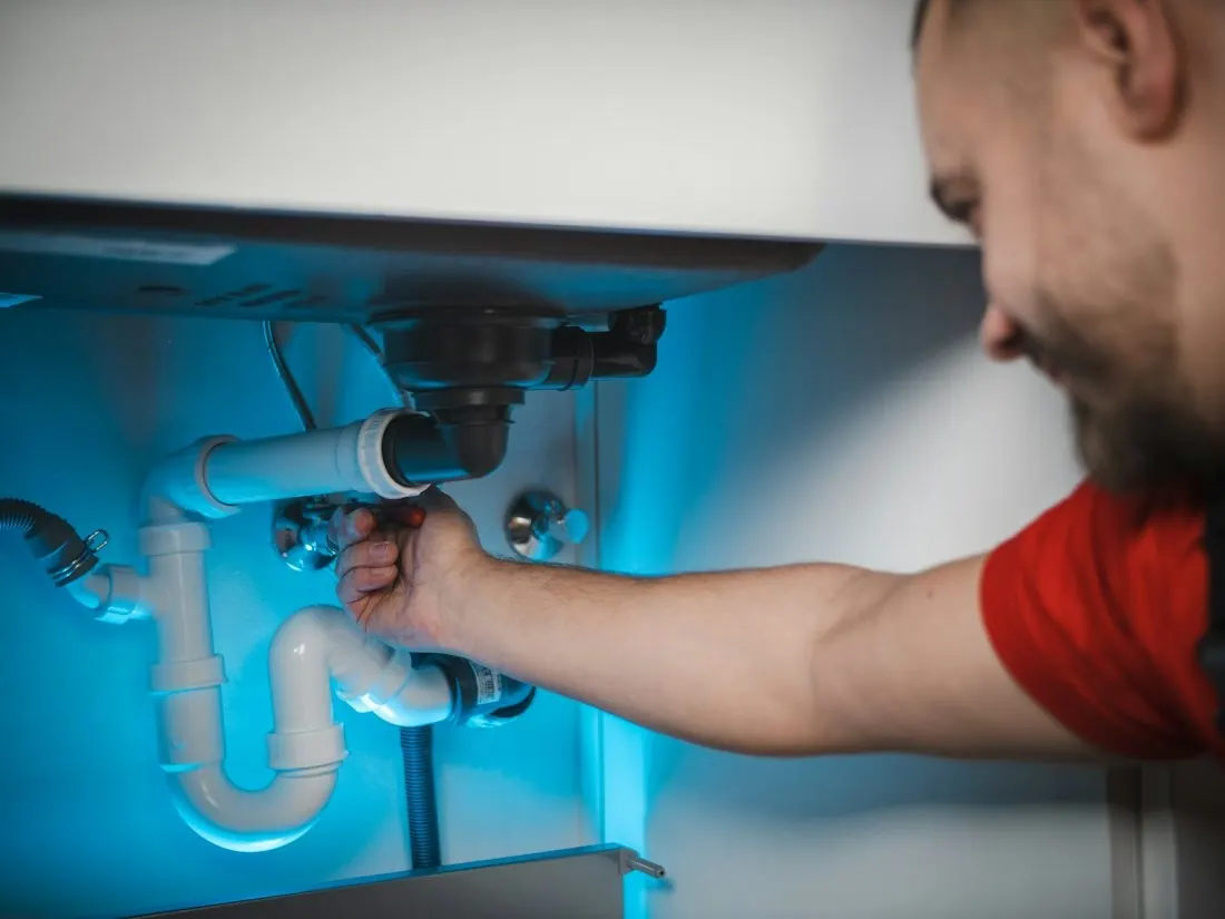 Un plombier remplace un siphon sous un évier.